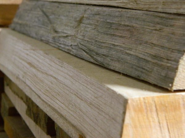 A close-up of stacked flat sawn split face bracewood, showing a light brown piece with clear grain and a darker, weathered piece with rough textures.
