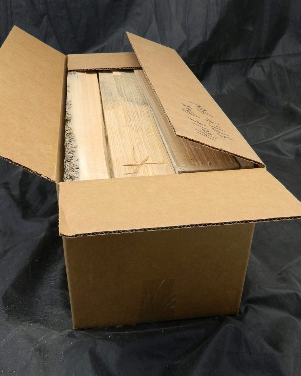 Open cardboard box filled with premium old-growth Sitka Spruce box Split Bracewood, showing light-colored, cut wood pieces, one with bark and another with a carved symbol.